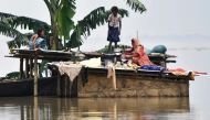 Members of an Indian family stand atop a hut at the flood affected area of Hatishila in Kamrup district of India's Assam state on July 16, 2019. AFP / Biju BORO