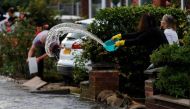 A woman uses a bowl to clear water from her drive to prevent rising flood water from entering her house in the Sale area of Manchester, Britain, July 31, 2019. Reuters/Phil Noble