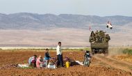 Syrian soldiers ride in the back of a truck past people sitting in a field with harvested aubergines, as government forces deploy for the first time in the eastern countryside of the city of Qamishli in the northeastern Hasakah province on November 5, 201
