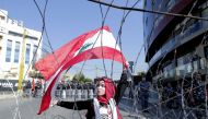 A Lebanese demonstrator waves the national flag while security forces stand by, during an anti-American protest near the US embassy in Awkar, northeast of the capital Beirut, on November 24, 2019. AFP / Anwar Amro