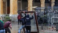 Anti-government protesters use a window as a makeshift shield as they confront security forces from behind a barbed-wire and metal fence barrier during clashes in the central downtown district of the Lebanese capital Beirut near the parliament headquarter