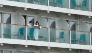 Passengers with face masks and bathrobes look out from a cabin of the World Dream cruise ship, after it had been denied entry in Taiwan amid concerns of coronavirus infection on board, at the Kai Tak Cruise Terminal in Hong Kong, China February 6, 2020. R