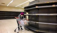 A shopper wearing a protective facemask sorts items in her trolley as she stands next to bare supermarket shelves, usually stocked with toilet paper and kitchen rolls, in Hong Kong on February 6, 2020. AFP / Philip Fong