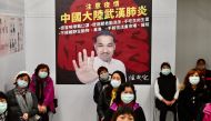 Mask-clad local residents wait in front of a poster showing New Taipei City mayor Hou You-yi during a drill organised by the New Taipei City government to prevent the spread of the COVID-19 coronavirus, in Xindian district on March 14, 2020. /AFP / Sam Ye