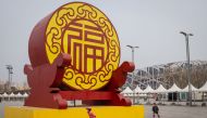 Children wearing face masks, amid concerns of the COVID-19 coronavirus, roller skate at the Olympic park outside the national 'Birds Nest' stadium (R, back), the site of the 2008 Beijing Olympics in Beijing on March 24, 2020. / AFP / NICOLAS ASFOURI