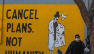 A man wearing gloves and a face mask walks by a mural reading 