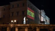 A woman jogs past the Greek parliament building in Athens, lighted with Spanish national flag colors supporting Spain in their efforts against the COVID-19 coronavirus on April 11, 2020. / AFP / Louisa GOULIAMAK