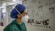:This photo taken on April 14, 2020 shows a staff member walking past graffiti encouraging people to defeat the COVID-19 coronavirus after all patients left Leishenshan Hospital in Wuhan in China's central Hubei province.  / AFP / STR