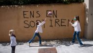 Jan, 5, looks at his sisters Ines, 11, and Mar (C), 9, playing in front of a graffit reading in Catalan 