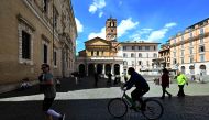 A man rides his bike as another jogs past Rome's Santa Maria in Trastevere square on May 3, 2020, during the country's lockdown aimed at curbing the spread of the COVID-19 infection, caused by the novel coronavirus.  AFP / Vincenzo PINTO
