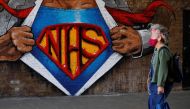 A woman wearing a facemask passes an artwork celebrating the National Health Service (NHS) painted on a brick wall in central London on May 5, 2020, during the nationwide lockdown due to the novel coronavirus COVID-19 outbreak. / AFP / Tolga AKMEN
