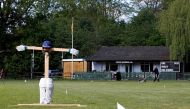 Gary O'Hara, volunteer groundsman and semi-retired player for Crown Taverners in the Hampshire cricket league, mows the grass on the ground in front of the club house with a cricket-themed scarecrow standing sentinal at Crown Taverners Cricket Club in Cam
