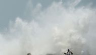 Men walk past as waves hit a breakwater at Kasimedu fishing harbour in Chennai on May 19, 2020, as Cyclone Amphan barrels towards India's eastern coast. / AFP / Arun SANKAR

