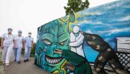 TOPSHOT - Medical staff members walk past a mural depicting a nurse, a doctor and a soldier fighting against the COVID-19 pandemic, painted by street artist Slimjoe in support of health workers, outside the Emilie Muller Hospital in Mulhouse, eastern Fran