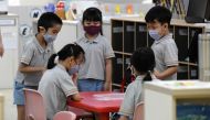 Children wearing face masks gather around a table inside their classroom as schools reopened in Singapore on June 2, 2020, as the city state eased its partial lockdown imposed to prevent the spread of COVID-19 in Singapore. / AFP / ROSLAN RAHMAN