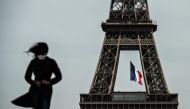 (FILES) In this file photo taken on May 11, 2020 a woman wearing a face mask walks as a French national flag flies on the Eiffel Tower in background in Paris on the first day of France's easing of lockdown measures in place for 55 days to curb the spread 