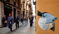 People pass near a drawing of a person wearing a mask in a wall, due to the coronavirus outbreak, in central Barcelona, Spain, March 12, 2020. REUTERS/Albert Gea