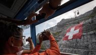 Tourists wearing a face mask take pictures of a huge 6400 meters square Swiss flag hanging on mountain Saentis on eve of Swiss national day on July 31, 2020 near Schw?galp, eastern Switzerland. Many Swiss stay in their country for holidays due to travel r