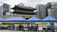 Health workers wearing protective clothing receive people at a temporary COVID-19 coronavirus testing station near Namdaemun (background), a 600-year-old gate listed as South Korea's number one national treasure, in Seoul on August 10, 2020. / AFP / Jung 