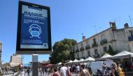 People wearing face masks walk next to a billboard reading: 