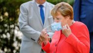 German Chancellor Angela Merkel takes off her face mask as she arrives for a family photo in front of the Staendehaus former parliament building prior to a North Rhine-Westphalian cabinet meeting on August 18, 2020 in Duesseldorf, western Germany. / AFP /