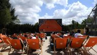 (FILES) In this file photo taken on May 29, 2019 people sit in sun loungers outside of the courts and watch on a giant screen the men's singles second-round match between Greece's Stefanos Tsitsipas and Bolivia's Hugo Dellien on day four of The Roland Gar