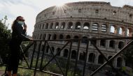 A woman wearing a face mask stands next to the Colosseum as Italy adopts new restrictions aimed at curbing a surge in the coronavirus disease (COVID-19) infections, in Rome, Italy October 13, 2020. Reuters/Guglielmo Mangiapane