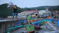 A resident holds onto his umbrella in strong wind as others stand by their wooden boats along the coastal area of Legaspi City, Albay province south of Manila on october 25, 2020, ahead of tropical storm Molave's expected landfall. / AFP / Charism SAYAT