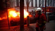 A firefighter runs past a burning car during a protest against the 