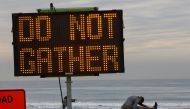 A woman stretches near a warning sign on the beach as new stay-at-home orders begin in Southern California during the outbreak of the coronavirus disease (COVID-19) in Oceanside, California, U.S., December 7, 2020. REUTERS/Mike Blake

