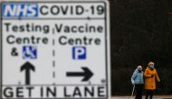 People walk behind a sign showing the way to the NHS Vaccination Centre and the testing centre parking lots, amid the coronavirus disease (COVID-19) outbreak, in Manchester, Britain January 11, 2021. REUTERS/Phil Noble/File Photo