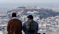 Two men sit on Lycabettus hill as the Parthenon temple is seen atop the Acropolis hill following snowfall in Athens, Greece, February 17, 2021. REUTERS/Vassilis Triandafyllou