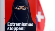 FILE PHOTO: A Swiss national flag flies behind a poster of the initiative committee against wearing the burqa (Verhuellungsverbot) reading 
