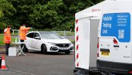 Staff members stand next to a car at a coronavirus disease (COVID-19) mobile testing unit at Oasis Beach Swimming Pool in Bedford, Britain May 25, 2021. Reuters/Paul Childs