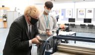 Britain's Prime Minister Boris Johnson (L) works the screen-pressing machine in the Arts and Design area during a visit to Kirklees College Springfield Sixth Form Centre in Dewsbury, West Yorkshire, Britain June 18, 2021. (Oli Scarff/Pool via REUTERS)