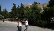 People without protective face masks make their way on the Areopagitou pedestrian street, as the ancient Parthenon temple is seen atop the Acropolis hill, following the easing of measures against the spread of the coronavirus disease (COVID-19) in Athens,