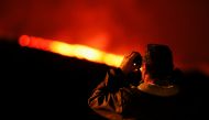 A man watches with binoculars the lava driven out by the Cumbre Vieja volcano from the viewpoint of Tajuya, on the Canary Island of La Palma, Spain, December 13, 2021. REUTERS/Borja Suarez