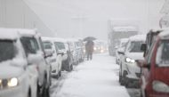 A person holding an umbrella walks among vehicles stuck in traffic in the Attiki Odos motorway, during heavy snowfall in Athens, Greece, January 24, 2022. REUTERS/Stelios Misinas