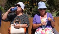 Women rest on a bench and drink water in hot weather during lunch hour in the financial district of Canary Wharf in London, Britain, July 15, 2022. (REUTERS/Kevin Coombs)