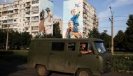 Ukraine servicemen drive past a mural of a family on damaged buildings in Bakhmut, in Donetsk region, Ukraine, August 14, 2022. (REUTERS/Nacho Doce)