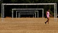 In this file photo taken on August 13, 2022 a woman walks in the heat past the goalposts on the scorched, dry grass on Hackney Marshes in London. (Photo by CARLOS JASSO / AFP)
