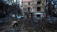 A serviceman collects fragments of missile in a crater left by a Russian strike in front of a residential building in the Ukrainian capita Kiev on December 31, 2022.  (Photo by SERGEI CHUZAVKOV / AFP)