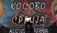 A pedestrian walks past a mural painting depicting the map of Kosovo with both cyrillic and english writing, reading 