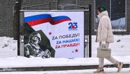 A woman walks past a poster dedicated to the upcoming Defender of the Fatherland Day which depicts a service member and reads 