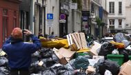 A pedestrian takes a picture of household waste containers in a street of Paris, on March 12, 2023, which have been piling up since collectors went on strike against the French government's proposed pensions reform on March 6, 2023. (Photo by Stefano RELLANDINI / AFP)
