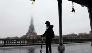 In this file photo taken on January 27, 2021 A woman rides a scooter in Paris in front of the Eiffel tower whose top disappears in the fog. Photo by Ludovic MARIN / AFP