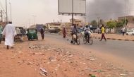 Smoke rises above buildings as people walk along a street in Omdurman on July 15, 2023. Since April 15, 2023, the forces the Sudanese army chief have been at war with the paramilitary Rapid Support Forces (RSF) paramilitary group. (Photo by AFP)
