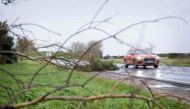 This photograph taken on November 2, 2023, in Courseulles-sur-mer, western France, show a car driving past a tree that has fallen on the road. (Photo by Lou Benoist / AFP)
