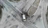 This aerial view shows a car passing a snow-covered road intersection close to Saint-Pierre-de-Plesguen, western France, on January 9, 2024. (Photo by Damien MEYER / AFP)