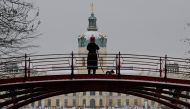 A woman walking her dog, stop to make a photo as she walks across a bridge overlooking the snow-covered gardens of Charlottenburg Palace as snow falls in Berlin on January 16, 2024. (Photo by John MACDOUGALL / AFP)